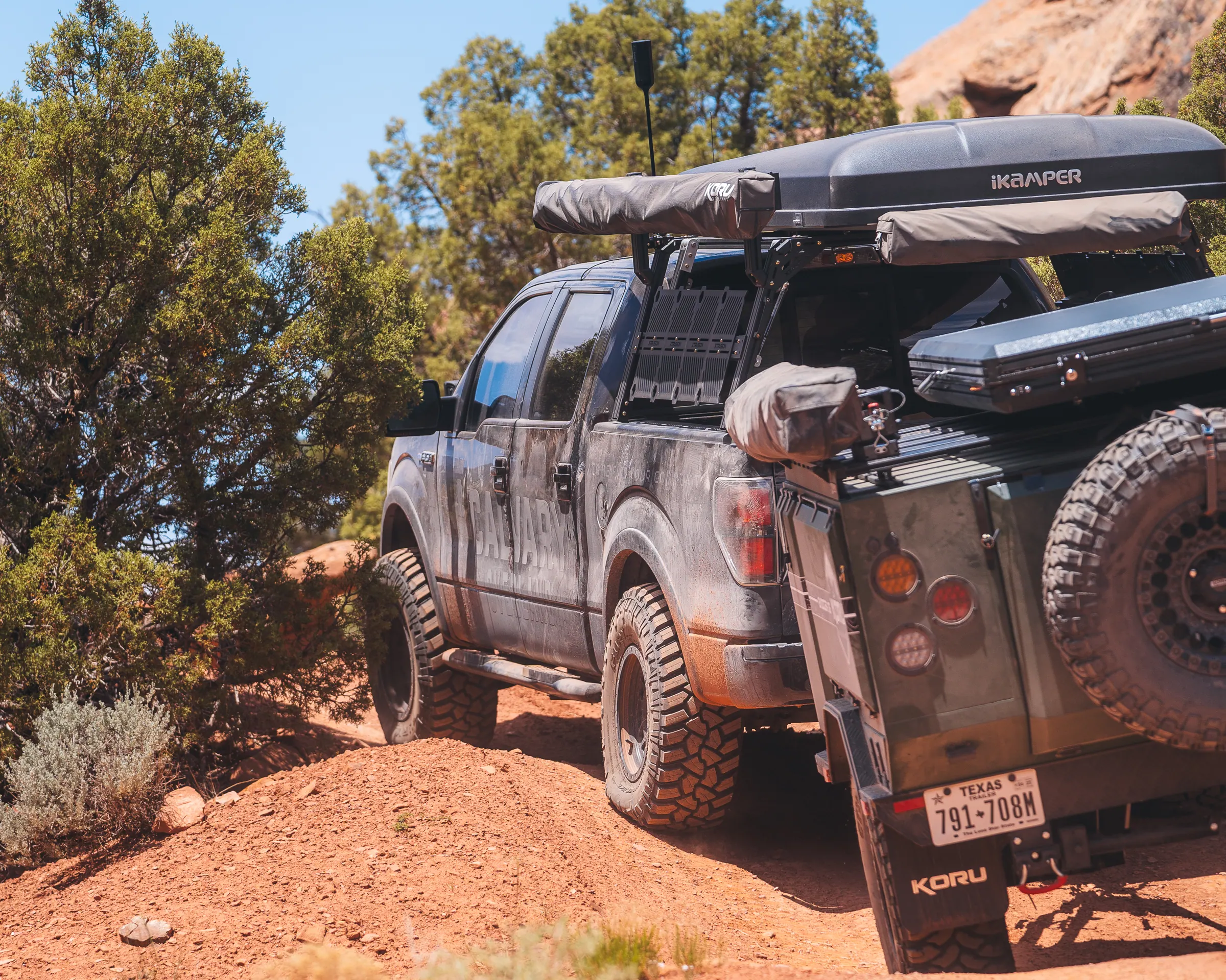 A pickup truck with a rooftop tent towing an overland trailer up a red dirt trail